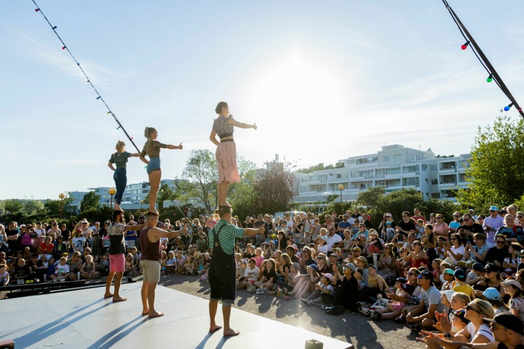 Kesäinen sirkustapahtuma, kuusi sirkustaiteilijaa lavalla ja yleisö edessä.