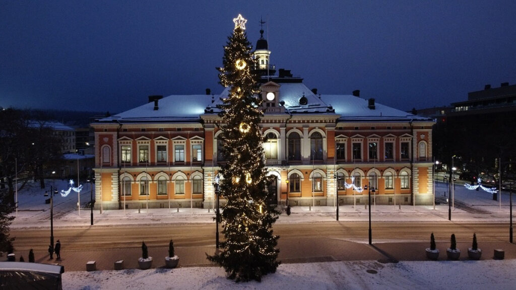 Kaupungintalo valaistuna pimeän aikaan, edustalla torikuusi jouluvaloineen.