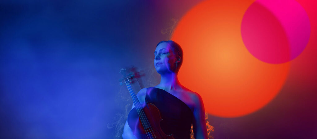 Kaupunginorkesterin muusikko sinisellä taustalla, jolla loistaa punainen valo.