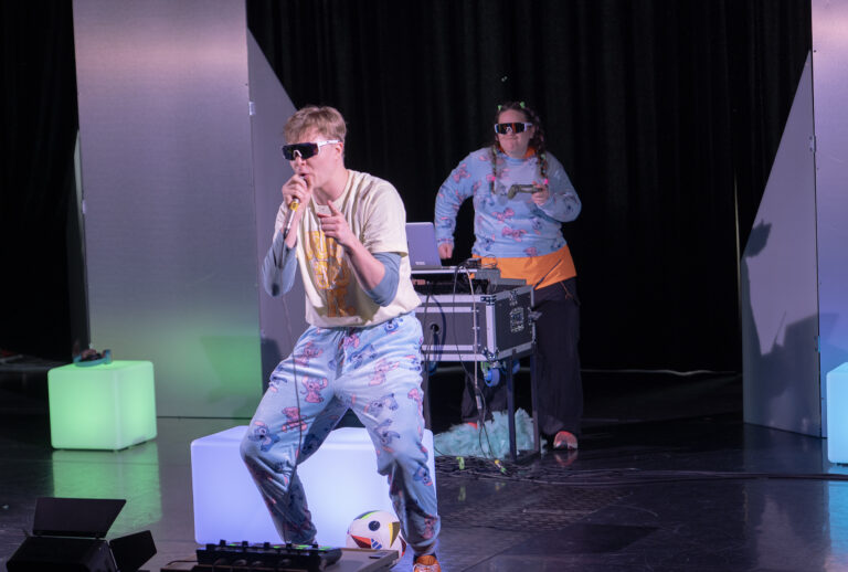 Kaksi hahmoa, joista toinen laulaa mikrofoniin ja toinen tanssii.