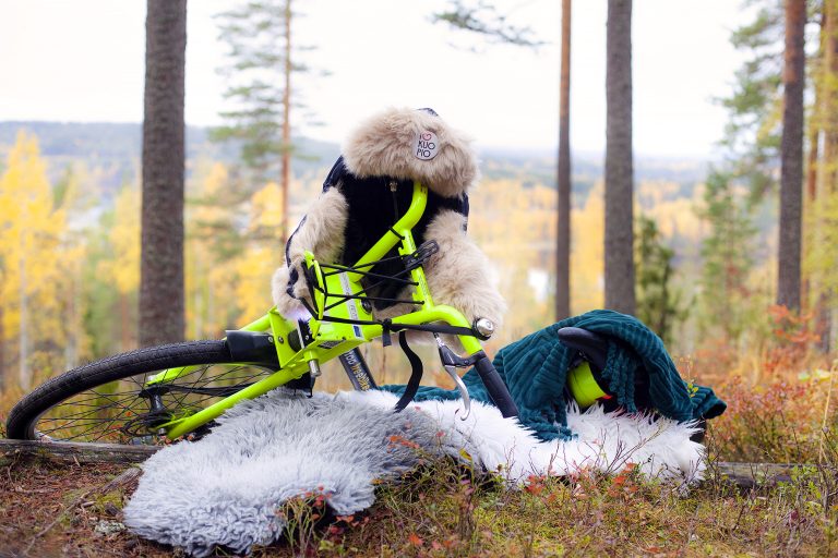 Syksyinen maisema taustalla, valkoinen talja, jonka päällä vihreärunkoinen pyörä kallellaan. Pyörän ohjaustangossa karvahattu.